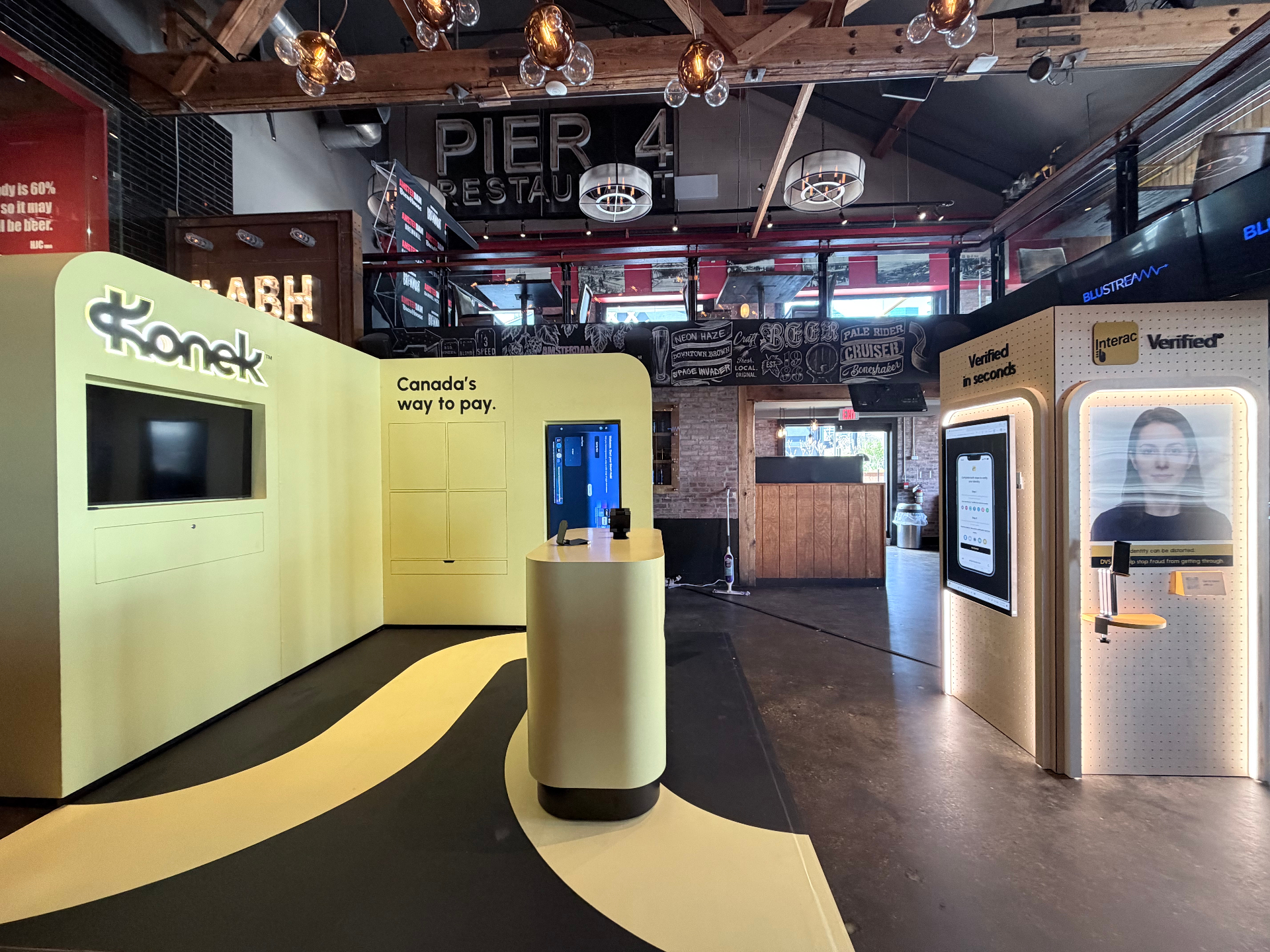 Konek Pier 4 takeover with chartreuse Konek wall, demo counter, and Interac Verified verification kiosks