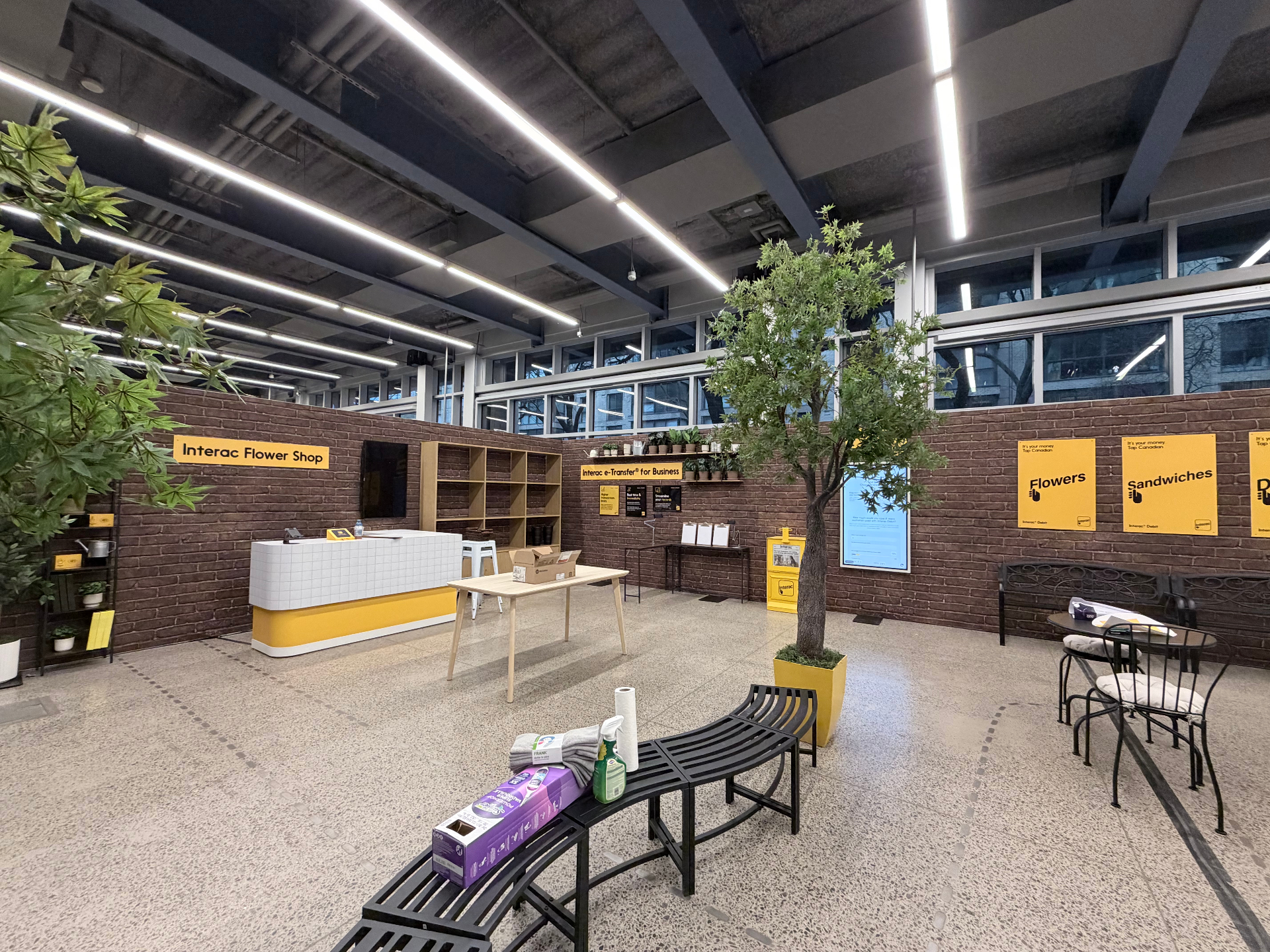 Wide view of the Interac merchant marketplace installation with flower shop counter, branded posters, and planted styling