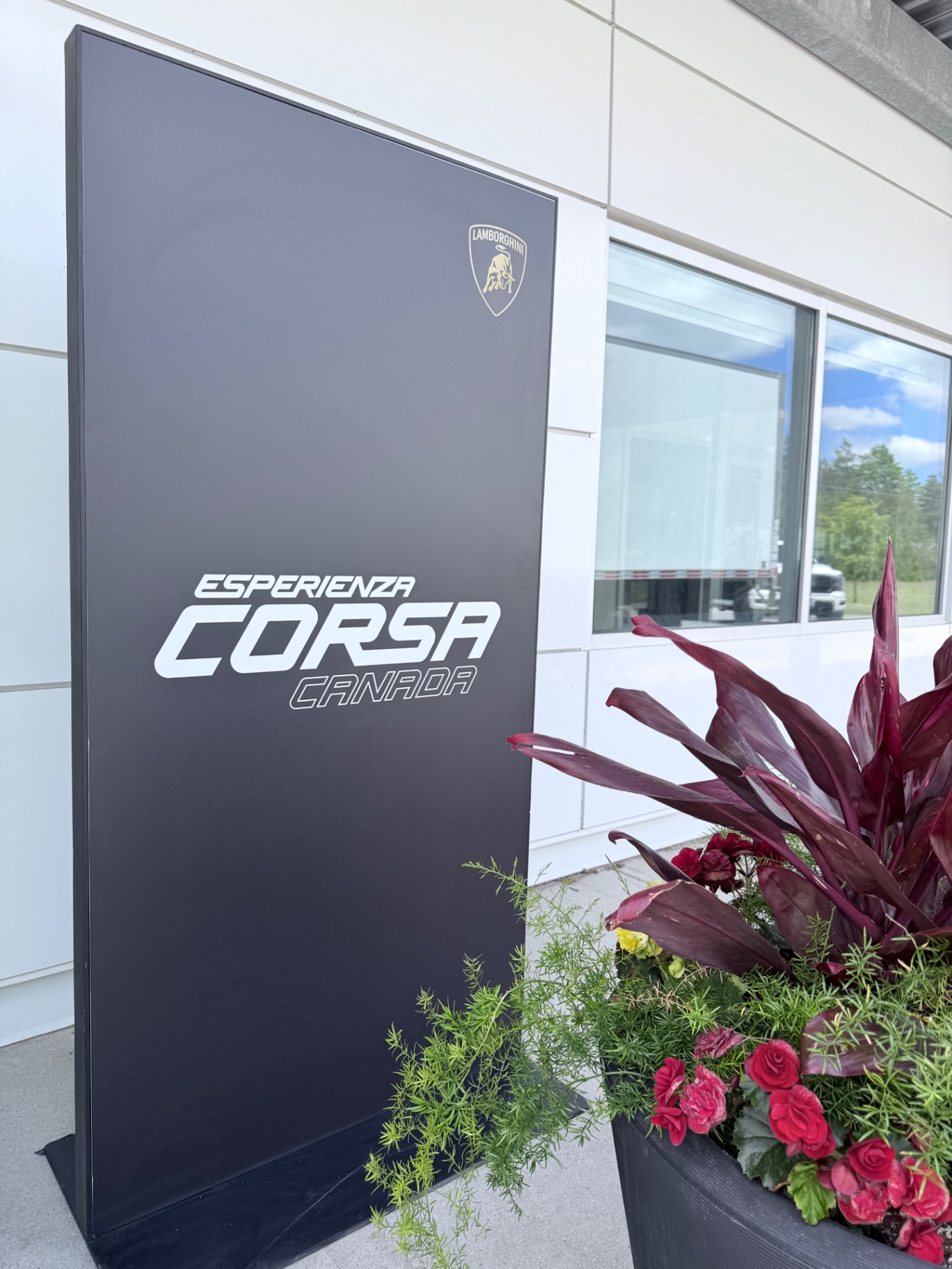 Esperienza Corsa Canada exterior monolith with Lamborghini shield beside lush planter at the clubhouse entrance